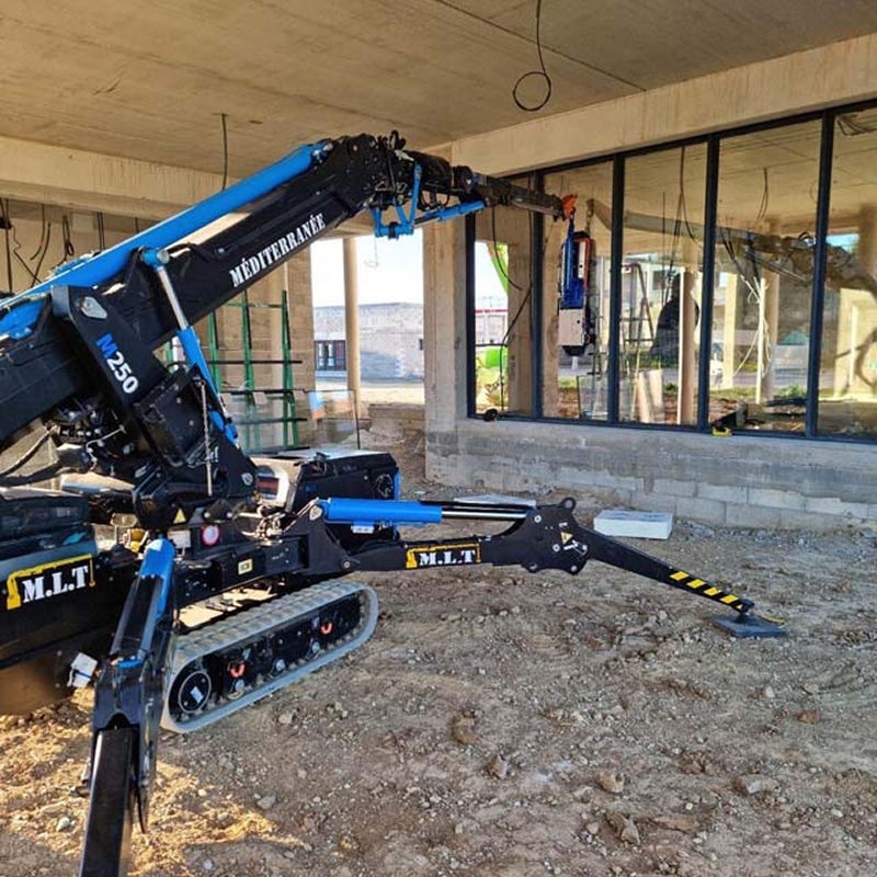 Grue araignée noire et bleue M.L.T M 250 "MÉDITERRANÉE" installant du verre sur un chantier, avec stabilisateurs étendus.