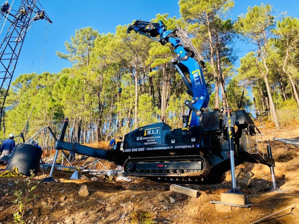 Mini-grue M.L.T. sur chenilles en action près d'un pylône en forêt. Levage sur terrain accidenté. Contact: 0695590680, mlt-mini-grue.fr.
