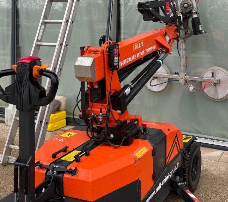 Mini-grue M.L.T orange manipulant un grand panneau de verre. Robot de levage Méditerranée Levage Transport pour installation de façade.