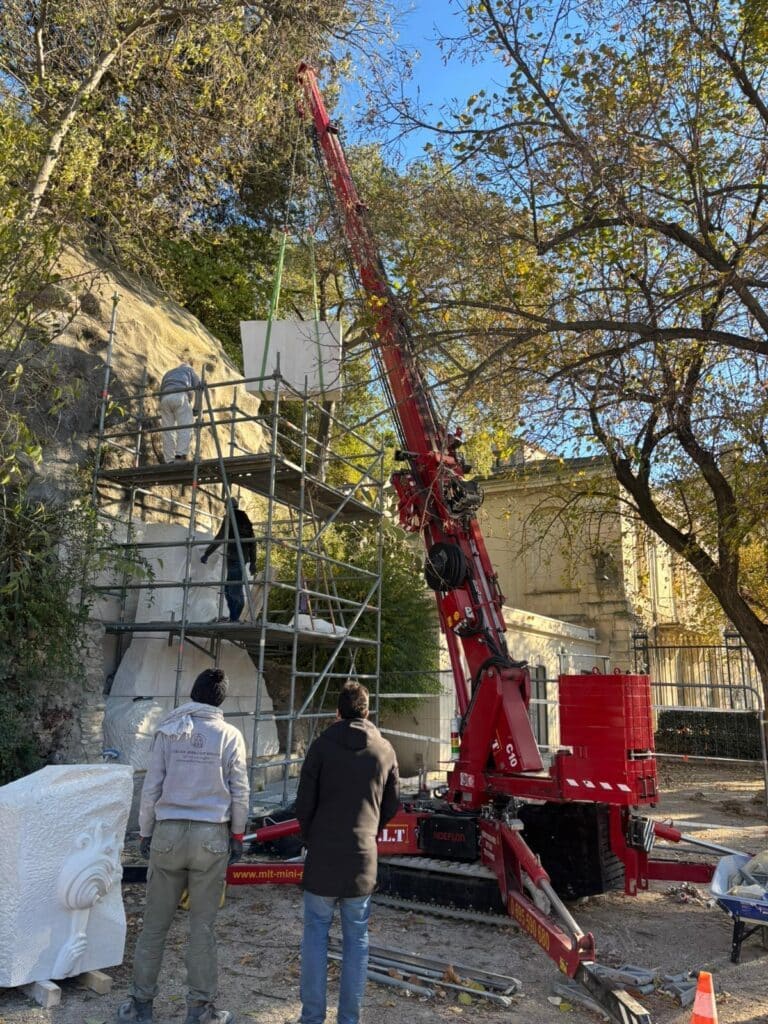 Grue compacte C10 soulevant un bloc de pierre pour la restauration d'une grande sculpture rocheuse. Sculpteurs sur échafaudage.