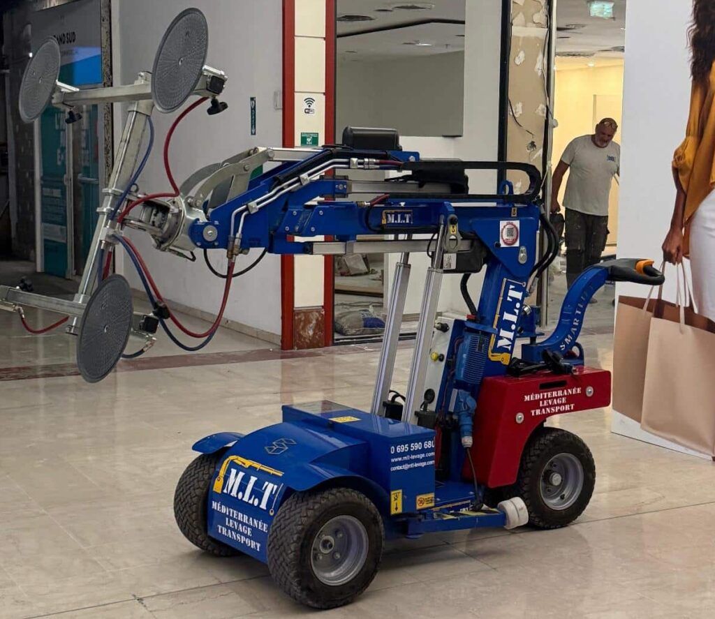 Robot lève-vitres M.L.T. (Méditerranée Levage Transport) bleu, équipé de ventouses, dans un magasin en rénovation. Tél. 0 695 590 680.