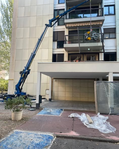 Grue araignée bleue levant un grand vitrage par ventouse vers un balcon d'un immeuble en rénovation.